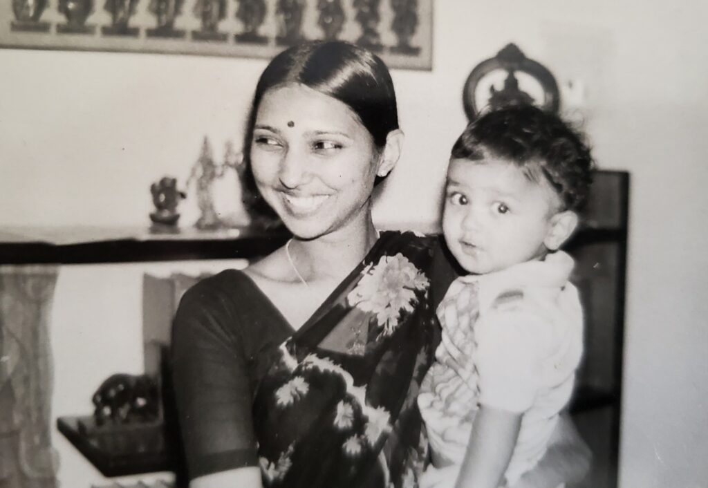 A smiling young woman in a saree holding a small child, vintage black and white portrait