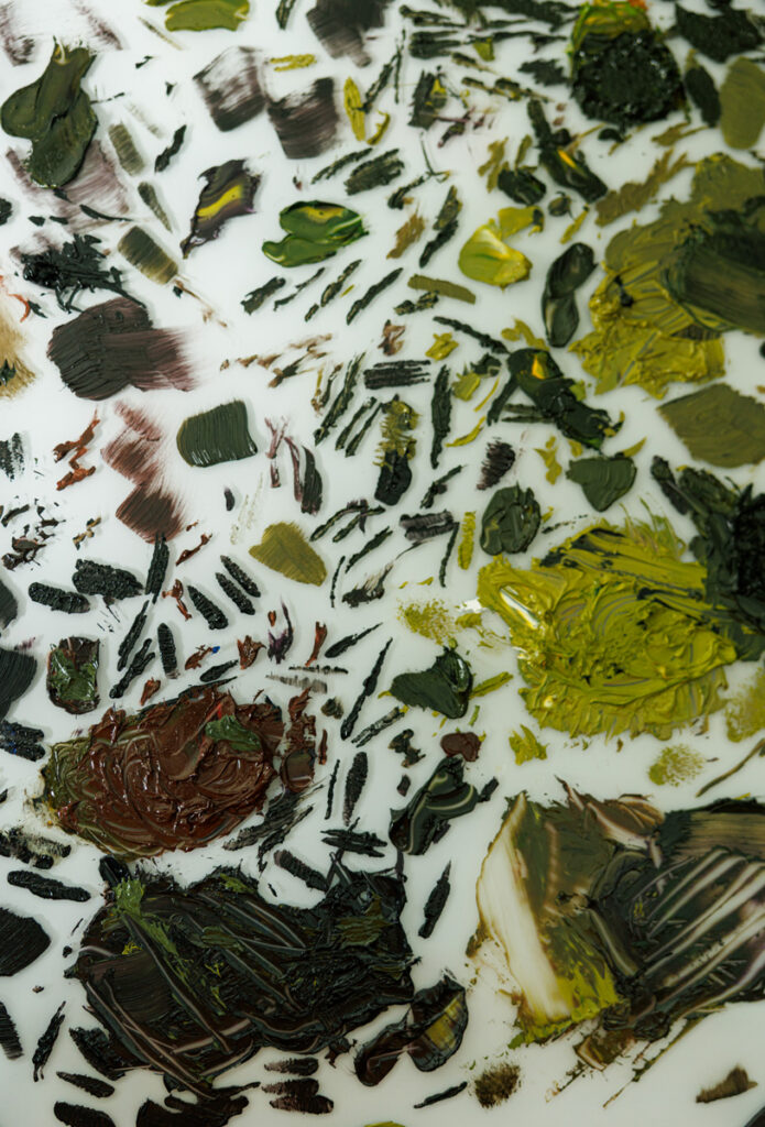 Close-up of an oil paint palette with mixed green and brown tones, used to hand-paint fine art portraits at Anj Portrait Studio in Des Moines
